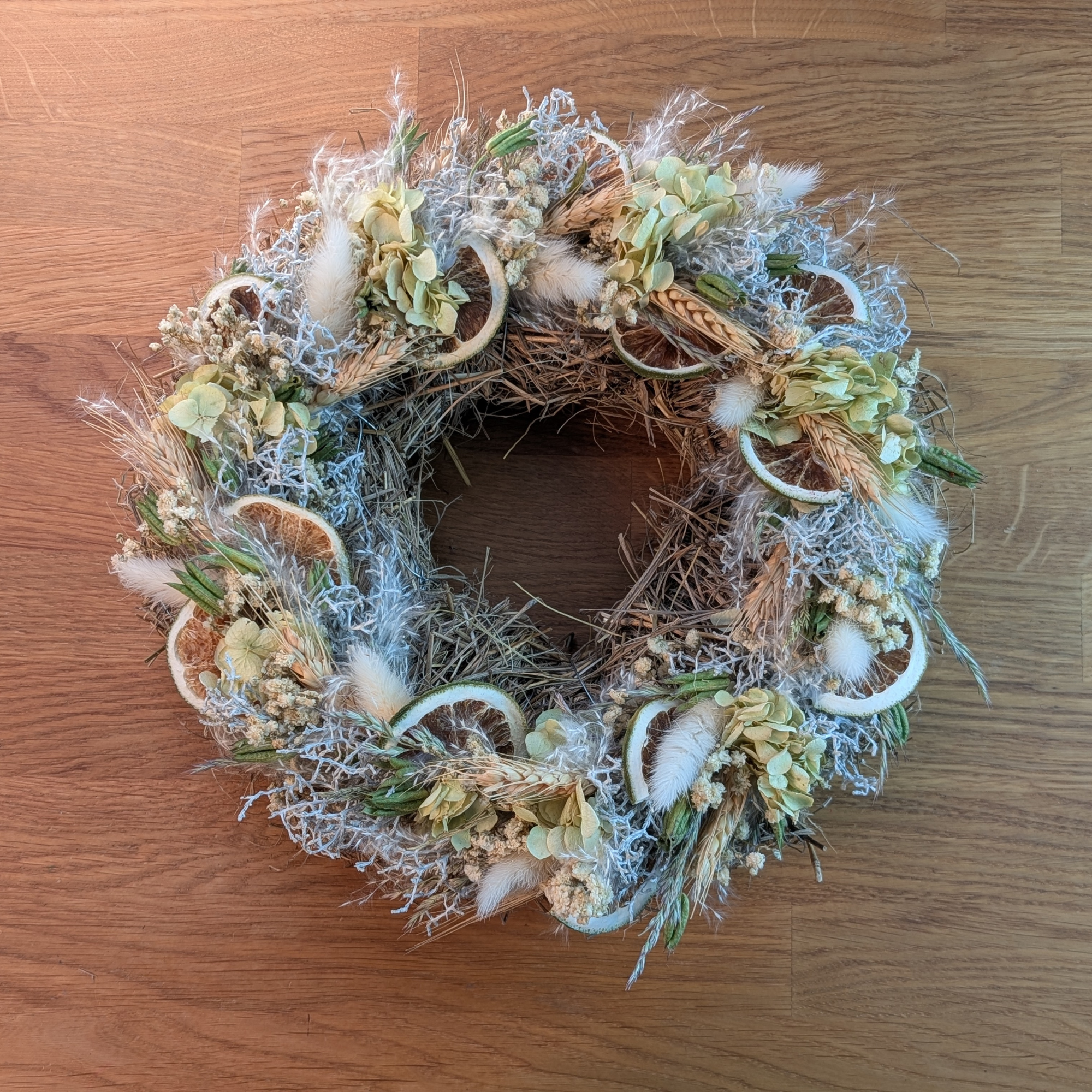 Trockenblumenkranz mit Limetten und Schleierkraut auf Strohunterlage